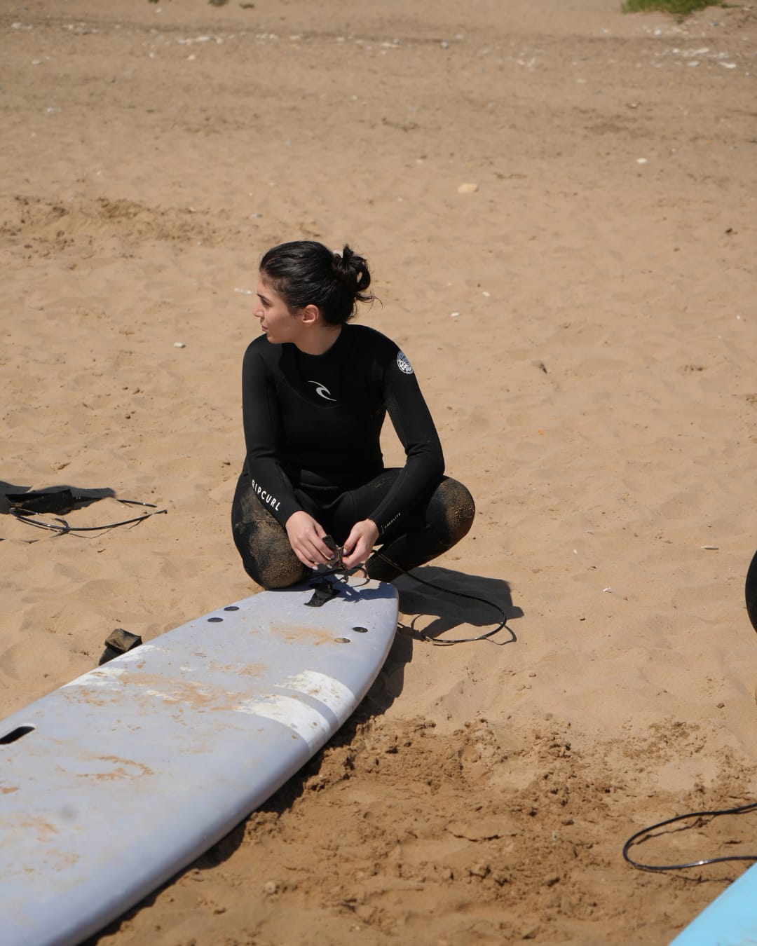 Surfer carrying her board in a wetsuit