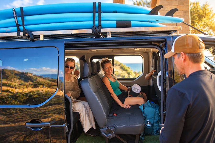 Guests smiling inside our van with surfboards on the roof